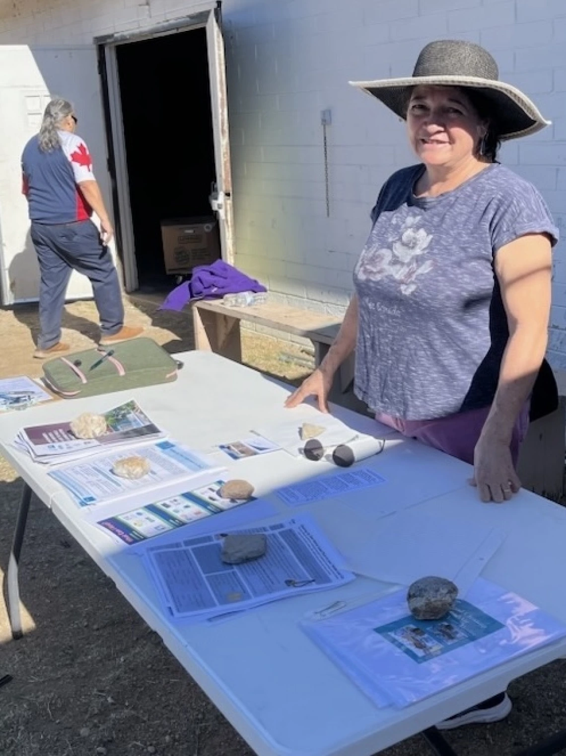 Photo of person in front of a building, smiling over a table with fliers