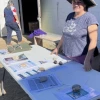 Photo of person in front of a building, smiling over a table with fliers